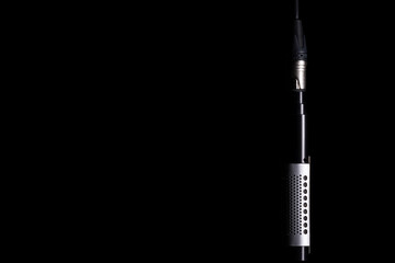 A ribbon microphone hanging from an XLR cable on a black background Nr.2
