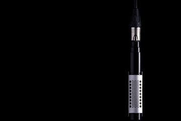 A ribbon microphone hanging from an XLR cable on a black background Nr.3