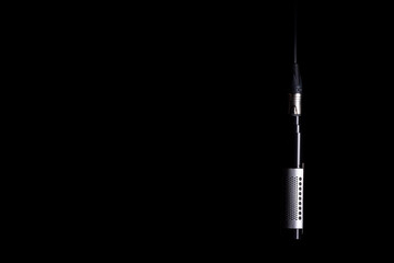 A ribbon microphone hanging from an XLR cable on a black background Nr.4