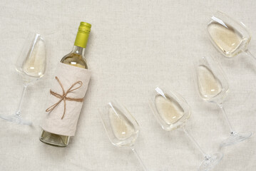 Fototapeta na wymiar Flat lay bottle and glasses with white wine. Beige linen tablecloth background. View from above.
