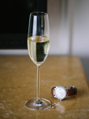 A narrow glass of champagne stands on the table, next to it lies a white gold wedding ring and a wristwatch.