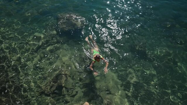 4k slow motion footage of sexy slim woman in green swimsuit swims to cliff on shore in clear turquoise water of mediterranean sea. vacation and wellness, Summer tourist Season Fethiye, Mugla Turkey