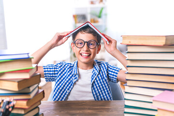 pretty happy schoolboy is sitting at home at his desk and reading books. Preparation of homework. Back to school. The boy enjoys learning and reads a lot of books. Self-education