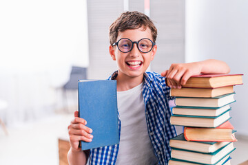 pretty happy schoolboy is sitting at home at his desk and reading books. Preparation of homework. Back to school. The boy enjoys learning and reads a lot of books. Self-education
