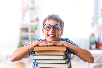pretty happy schoolboy is sitting at home at his desk and reading books. Preparation of homework. Back to school. The boy enjoys learning and reads a lot of books. Self-education