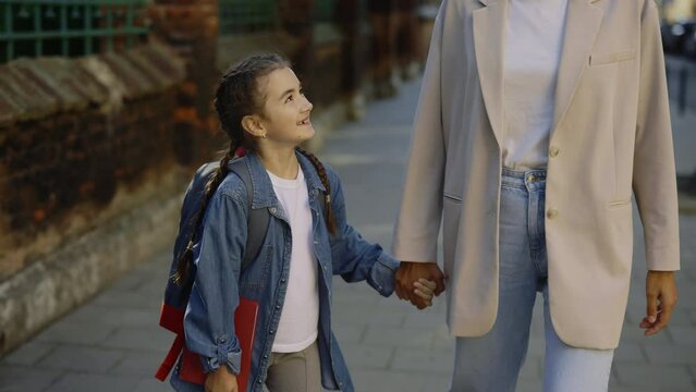 Portrait of happy schoolgirl holding mothers hands. Female parent and kid wanking on the street talking and smiling. Family relationship concept. Front view. Close up