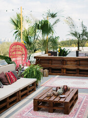 Table and sofa made of pallets on the terrace. There are lots of succulents and candles on the...