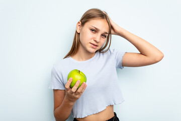 Young caucasian girl holding an apple isolated on blue background being shocked, she has remembered important meeting.