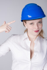Young female engineer wearing a blue hard hat is pointing to that hat