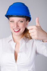 Young female engineer wearing a blue hard hat shows thumbs-up