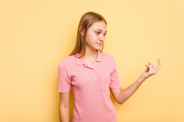 Young caucasian girl isolated on yellow background pointing with finger at you as if inviting come closer.