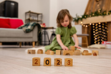Wooden cubes with the numbers 2023 stand on the floor in a row. Background of blurred unhappy girl