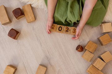 Top view of girl who holds wooden cubes with the numbers 2023 in her hands. Lifestyle Active game