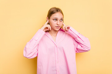 Young caucasian girl isolated on yellow background covering ears with fingers, stressed and desperate by a loudly ambient.