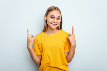 Young caucasian girl isolated on blue background indicates with both fore fingers up showing a blank space.