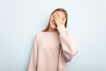 Young caucasian girl isolated on blue background laughs joyfully keeping hands on head. Happiness concept.