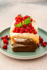 Rich sweet pie with fresh fruits, decorated with red currants and raspberries, in a plate on a pink background