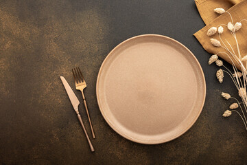 Table setting, empty plate and cutlery on a brown background, top view of the served table...