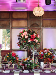 Fototapeta na wymiar Exotic wedding banquet table decor in purple. Tropical flowers decor, carved chandelier, purple wine glasses, crockery, cutlery.