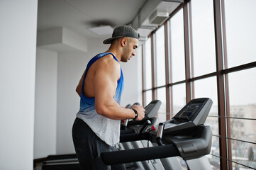 Fit and muscular arabian man running on treadmill in gym.