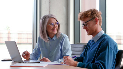 Senior grey-haired mature female teacher, executive or mentor helping young man student, new...