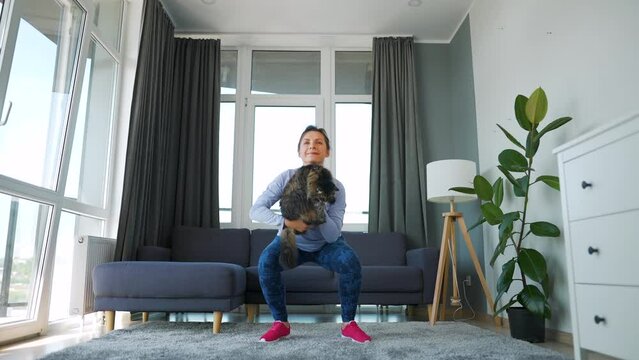 Woman squats with a cat in her arms. Home workouts.