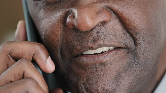 Unknown half face part old wrinkled emotional businessman African mature man talking on mobile phone unrecognizable boss negotiating with smartphone extreme closeup male mouth lips talk slow motion