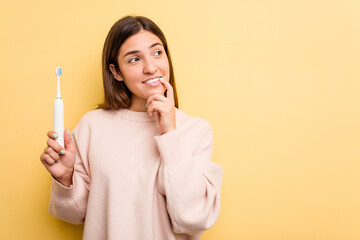 Young caucasian woman holding a electric toothbrush isolated on yellow background relaxed thinking about something looking at a copy space.