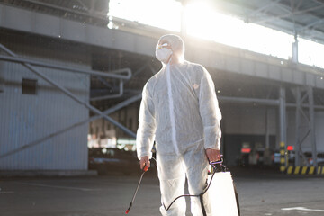 Fototapeta na wymiar Man dressed white protective overalls spraying surface antibacterial sanitizer sprayer during quarantine