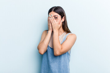 Young caucasian woman isolated on blue background blink through fingers frightened and nervous.