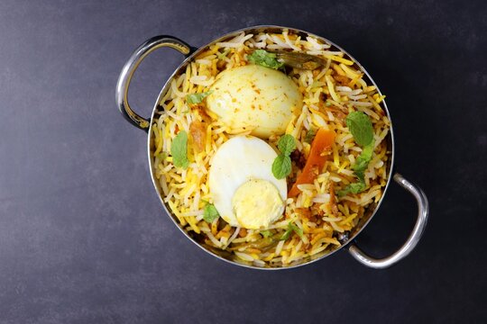 Egg dum Biryani or anda biryani Fragrant Basmati rice cooked with spicy masala gravy along with spices, veggies and boiled eggs. served with yogurt, salad and salan. Black background with copy space.