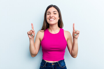 Young caucasian woman isolated on blue background indicates with both fore fingers up showing a...