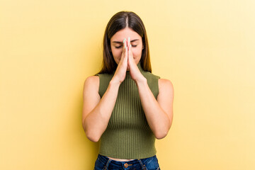 Young caucasian woman isolated on yellow background holding hands in pray near mouth, feels confident.