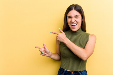 Young caucasian woman isolated on yellow background pointing with forefingers to a copy space,...