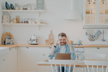 Happy young businessman in casual clothes working with computer at home