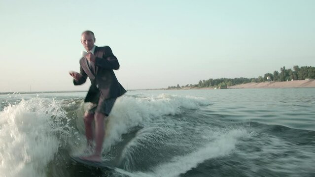 A surfer jumping on a wakeboard in a suit with a cup of tea or coffee in his hands. An experienced wakeboarder sprays water drops into the camera.