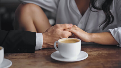 cropped view of man and woman holding hands near cup of coffee on kitchen table.