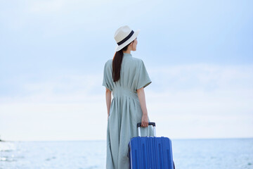スーツケースを持って海辺に佇む日本人女性