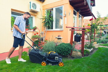 Young gardener mowing the lawn with lawnmower in summer