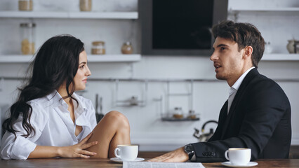 businessman talking with smiling girlfriend in white shirt near cups of coffee.