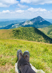 Hiking boots on the legs of the resting tourist with the characteristic peak of Mala Fatra - Velky Rozsutec. - 519143041