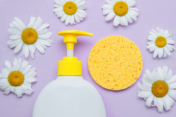 Plastic cosmetic white bottle with yellow dispenser and sponge, chamomile flowers close-up with empty space for text, conscious space, on purple background, flat lay,  concept of skin, face, body care