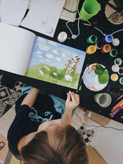 A boy sitting on the table painting and drawing a picture for school. Homeschooling, homework, kids art and hobby. Children talents development, elementary school