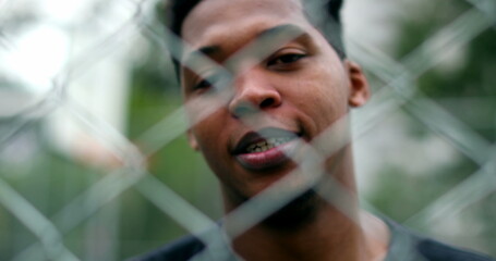Happy black African man smiling and laughing with metal fence in foreground