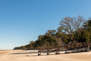 Old pier, now deck, on the sands of Kiyu beach, with the trees on the ravines of the coast, in San...