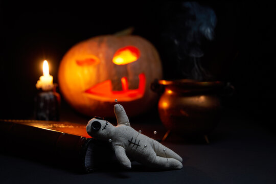 Halloween pumpkin with burning mouths, book and a voodoo doll - volt on dark background.