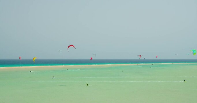 Kitesurfing on the tropical beach of Playa Del Mal Nombre, Fuerteventura, Canary Islands. People engaged in kiteboarding turquoise sea. The men on the board swims fast on the waves in shallow water.