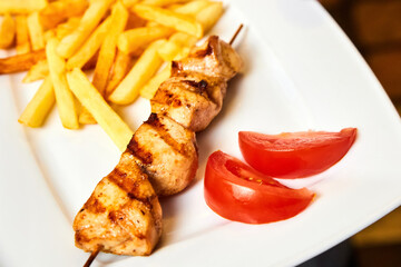 Chicken skewers with french fries and tomatoes on a white plate