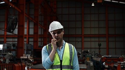 One man specialists inspect commercial, Wear safety uniform work with a radio at metal industry factory. Handsome caucasian worker in protective working clothes and with white helmet on head leaning.