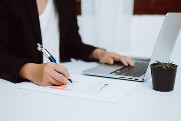 Close-up of businesswoman or accountant holding pen working with document and laptop computer on...